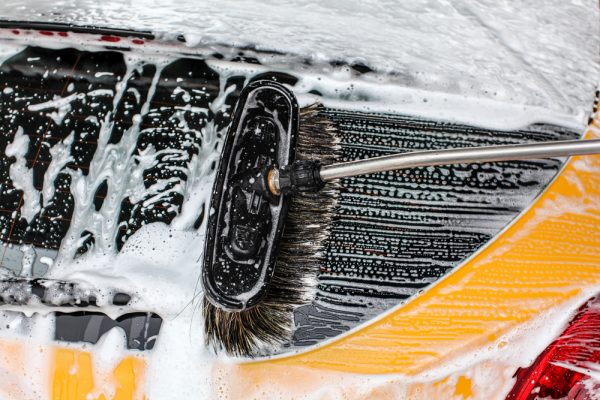 Detail of dark yellow car rear window washed in carwash. Brush leaving strokes in white soap and shampoo foam.